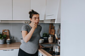 Pregnant woman in kitchen trying food