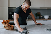 Man in kitchen wiping kitchen worktop