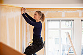 Female painter taping ceiling before painting