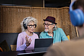 Senior couple sitting in cafe talking while working on digital tablet