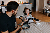 Vater füttert behindertes Kind im Rollstuhl am Küchentisch