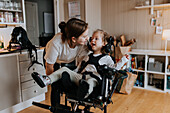 Mutter kümmert sich um behindertes Kind im Rollstuhl zu Hause
