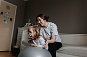 Mother supporting disabled child on fitness ball