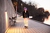 Young boy skateboarding at evening by the river and looking away