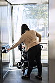 View of woman on parental leave with pram pushing button inside lift