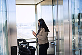 Smiling woman on parental leave with pram using cell phone inside lift