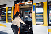 Mittlere erwachsene Frau am Bahnhof steigt mit Kinderwagen in den Zug ein