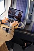 Mittlerer Ausschnitt einer Frau mit Laptop während einer Zugfahrt