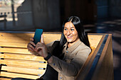 Lächelnde Frau sitzt auf dem Rücken im Bahnhof und macht ein Selfie