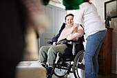 Mutter hilft behinderter Tochter im Rollstuhl beim Anziehen der Jacke