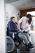 Mutter hilft behinderter Tochter im Rollstuhl beim Anziehen des Mantels