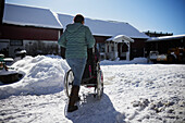 Rückansicht einer Frau, die bei einem Winterspaziergang eine Person im Rollstuhl schiebt