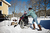 Rückansicht einer Frau, die bei einem Winterspaziergang eine Person im Rollstuhl schiebt