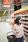 Frau schaut beim Einkaufen im Supermarkt auf die Preise während der Inflation