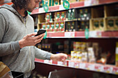 Man in supermarket comparing prices during inflation on cell phone