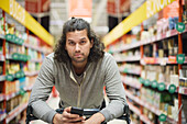 Man in supermarket holding cell phone and looking at camera