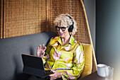 Ältere Frau mit Kopfhörern führt Videogespräch auf Tablet