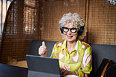 Ältere Frau mit Kopfhörern bei einem Videogespräch auf einem Tablet