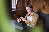 Älterer Mann mit Kopfhörern an Telefon und Tablet