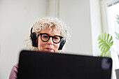 Smiling senior woman sitting withe headphones on and using laptop