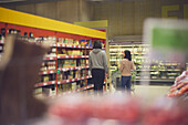 Rückansicht eines Paares, das im Supermarkt vor den Regalen steht und gemeinsam einkaufen geht