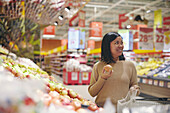 Lächelnde Frau steht im Supermarkt und hält einen Apfel