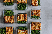 Overhead view of lunch boxes with lasagna and green beans as part of healthy meal prep