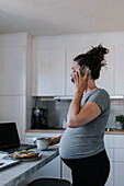Schwangere Frau telefoniert bei der Arbeit von zu Hause aus