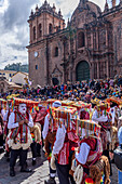 Cusco, a cultural fiesta, people dressed in traditional colourful costumes with masks and hats, brightly coloured streamers, in the Cusco central square by the cathedral. 
