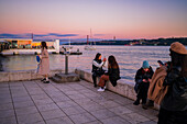Menschen genießen den Sonnenuntergang an der Promenade von Belem am Fluss Tejo, Lissabon, Portugal