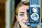 Porträt einer jungen schönen kaukasischen Frau in den 20ern mit blauen Augen beim Fotografieren mit einer alten Vintage-Kamera auf einem Stativ im Freien. Lifestyle-Konzept.