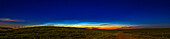 Ein Panorama nachtleuchtender Wolken in nordwestlicher Richtung kurz vor Mitternacht am Abend des 10. und 11. Juli 2022 über einem Hügel und einer roten Landstraße in Süd-Alberta, Kanada.