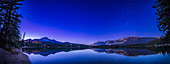 A panorama of Lake Edith in Jasper National Park, Alberta, on a calm autumn night, looking north to the stars of Ursa Major, the Great Bear, and the Big Dipper in deep twilight. Arcturus is at far left setting in the northwest over Pyramid Mountain, while Capella in Auriga and the stars of Perseus are rising at right in the northeast. This was on a mid-October night when the Big Dipper rides low in the northern sky from this latitude of 53° N.