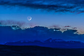 Die zunehmende, zwei Tage alte Mondsichel geht am 6. April 2019 vom Rothney Astrophysical Observatory aus gesehen über dem Gebirgszug der Rocky Mountains in Süd-Alberta unter. Der Erdschein ist auf der Nachtseite des Mondes zu sehen.
