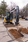 A utility worker uses a track hoe to excavate a hole in the street to repair a utility line in a neighborhood.