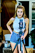 Portrait of a young beautiful caucasian woman in her 20´s with blue eyes photographing with an old vintage camera on a tripod outdoor. Lifestyle concept.