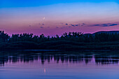 Die zunehmende Mondsichel zwei Tage nach Neumond an einem rauchigen Himmel und über dem Red Deer River im Dinosaur Provincial Park in Alberta, Kanada. Das war am 30. Juni 2022. Trotz des dunstigen Himmels zeigen sich die Farben der Dämmerung gut am Himmel und spiegeln sich im Wasser. Auf der Nachtseite des Mondes ist das Glühen des Erdscheins leicht zu erkennen. Castor und Pollux in den Zwillingen sind rechts schwach zu erkennen.
