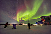 A group of aurora fans are watching and shooting the Northern Lights at the Churchill Northern Studies Centre in Churchill, Manitoba on February 27, 2022. On this night the most active part of the display was to the west, best seen from out in the parking lot. The stars of Taurus are at left.