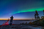 Der Fotograf Stephen Bedingfield bereitet sich auf die Aufnahme des Nordlichts am Prelude Lake in der Nähe von Yellowknife, NWT, am 9. September 2019 vor. Sogar am Dämmerungshimmel beginnt ein Polarlichtbogen zu erscheinen.