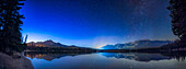 A panorama of the northern stars in autumn over and reflected in the calm waters of Lake Edith in Jasper National Park, in the deep twilight. The Big Dipper and Ursa Major are at left, with Arcturus over Pyramid Mountain at far left. Capella is rising at right, and above it are the stars of Perseus and Cassiopeia. This was on a very clear mid-October night in 2022.