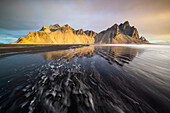 Spiegelung des Berges Vestrahorn über schwarzem Sand bei Sonnenaufgang im Frühling, Halbinsel Stokksnes, Hofn, Austurland, Island, Polarregionen