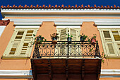 Low-angle view of a traditional house with closed wooden shutters and a balcony with plant pots against a blue sky in Nafplion, Peloponnese, Greece, Europe