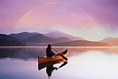 USA, St. Armand, Rear view of woman canoeing on calm Lake Placid at sunset in Adirondack Park