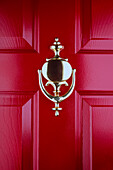 Nahaufnahme eines altmodischen Messing-Türklopfers an einer roten Haustür