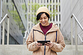 Lächelnde Frau hält digitales Tablet auf Stufen in der Stadt