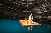 Portrait einer Frau auf einem Schwimmdock in der Nähe der Felsenküste sitzend