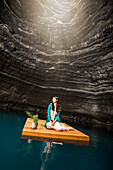 Woman sitting on floating dock near rocky coast