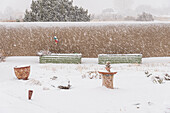 USA, New Mexico, Santa Fe, Garten mit Lehmmauer und Blumentöpfen bei starkem Schneefall