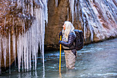 USA, Utah, Springdale, Zion National Park, Senior woman looking at icicles while hiking in mountains