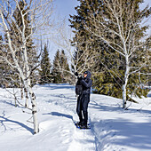 USA, Idaho, Sun Valley, Senior woman wearing snowshoes hiking in snowy forest